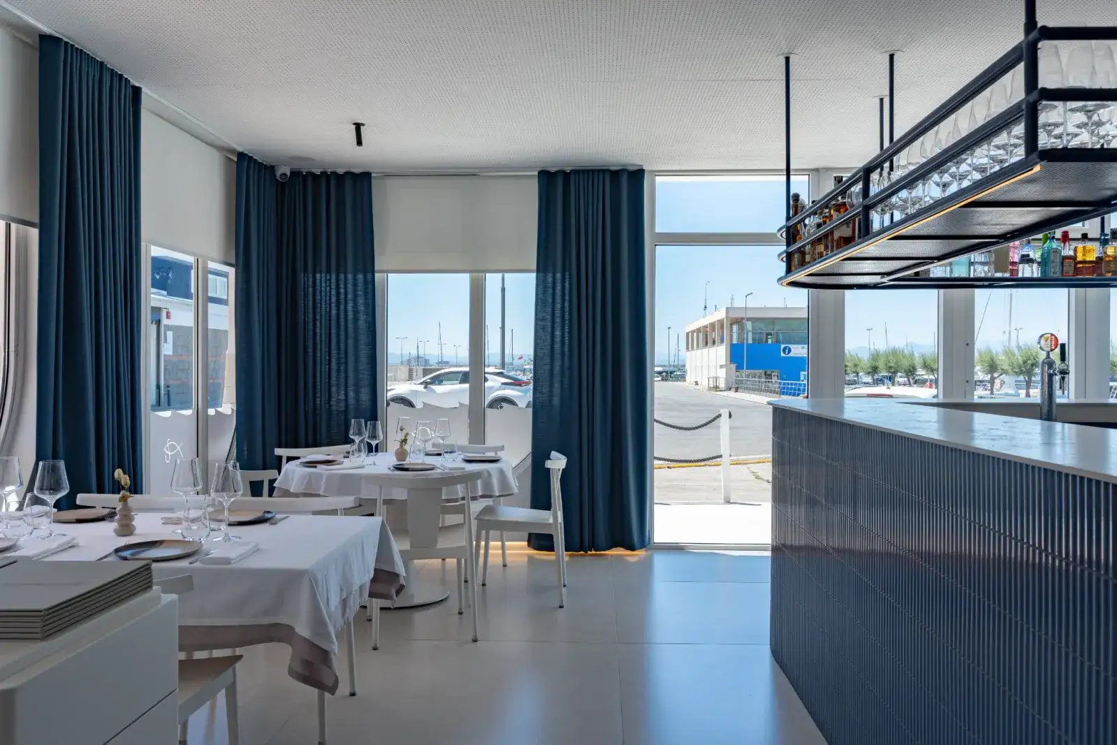 Sala interior de Restaurant La Llotja en España, comedor luminoso con manteles blancos y vistas al puerto mediterráneo
