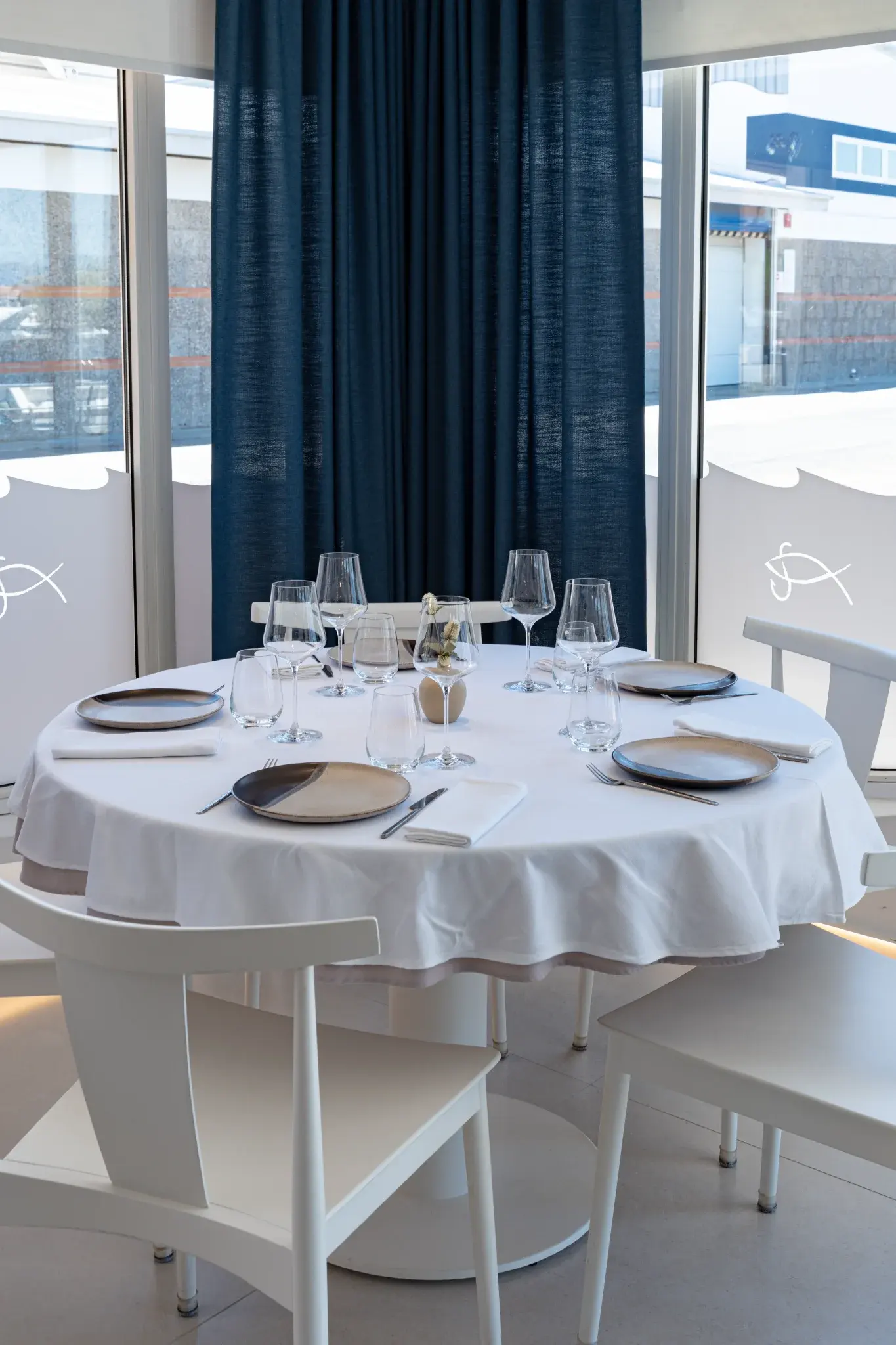 Mesa redonda elegantemente montada con mantelería blanca en Restaurant La Llotja, comedor luminoso en España