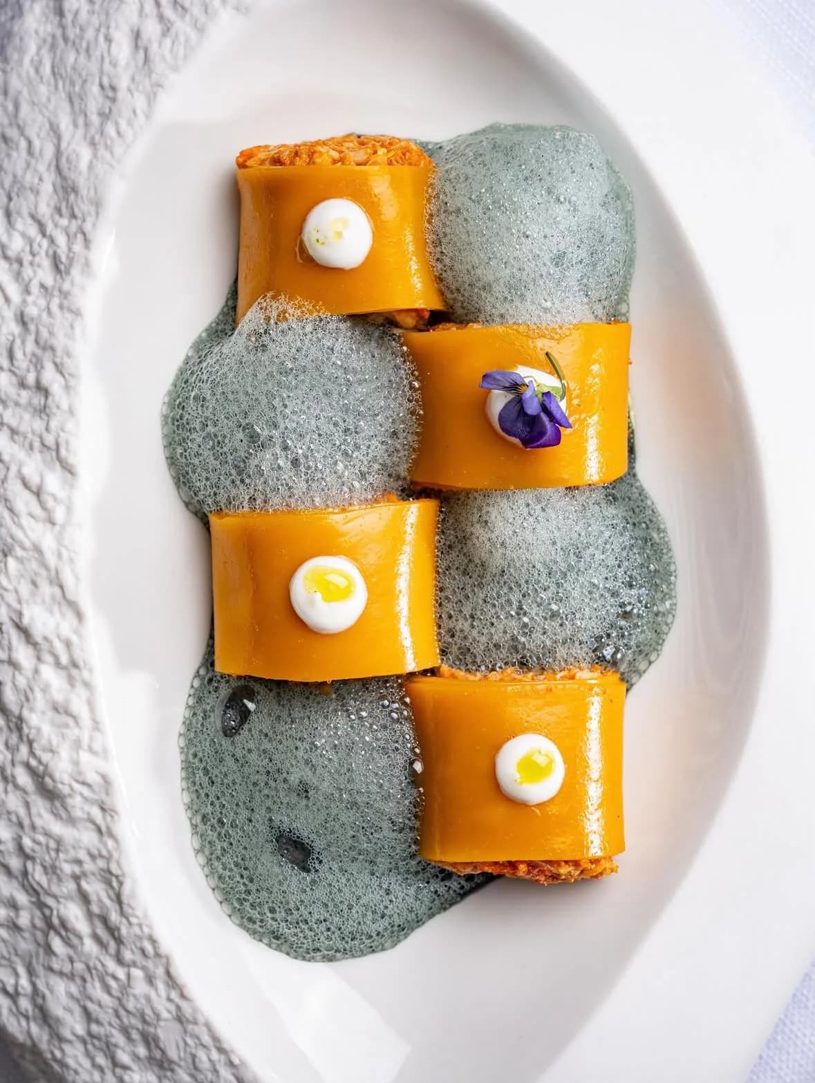 Ravioli de gamba y vieira con espuma y flores comestibles en plato blanco en La Llotja espai gastronòmic, Port de Roses