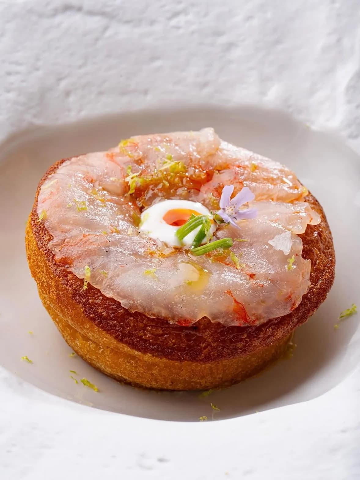 Tartaleta crujiente cubierta de gamba roja cruda y crema en plato blanco en Restaurant La Llotja, cocina mediterránea en España